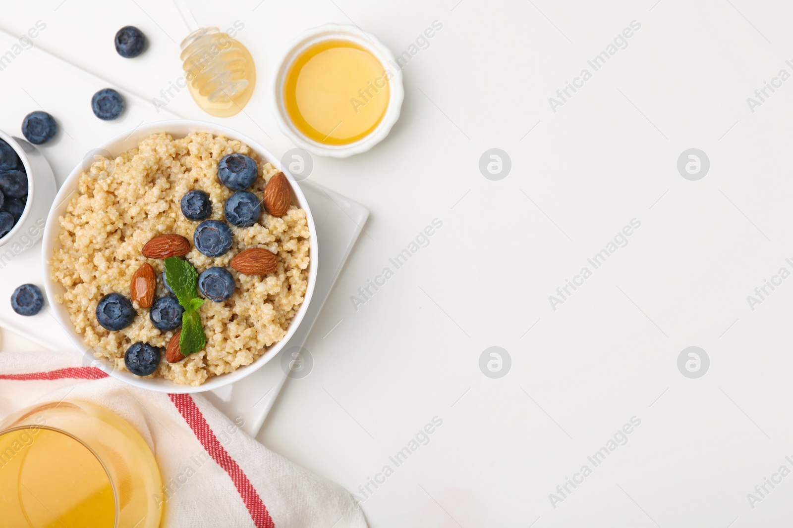 Photo of Bowl of delicious cooked quinoa with almonds and blueberries on white table, flat lay. Space for text