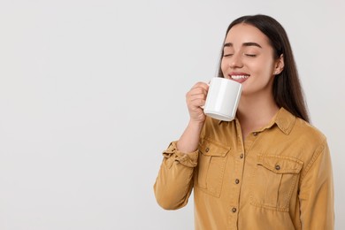 Photo of Happy young woman drinking beverage from white ceramic mug on light grey background, space for text