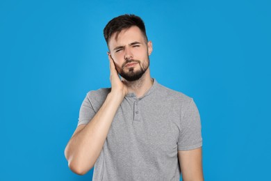 Young man suffering from ear pain on light blue background