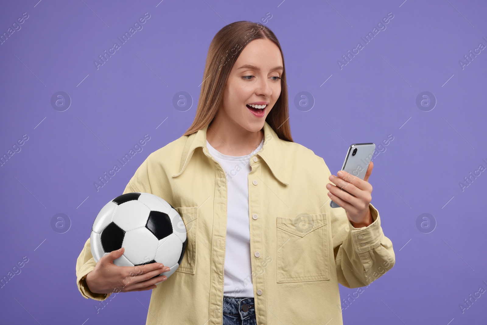 Photo of Emotional sports fan with ball and smartphone on purple background