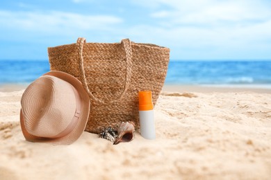 Image of Bag with sunscreen and hat on sunny ocean beach, space for text. Summer vacation