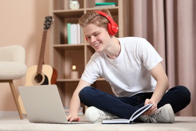 Online learning. Smiling teenage boy with book typing on laptop at home