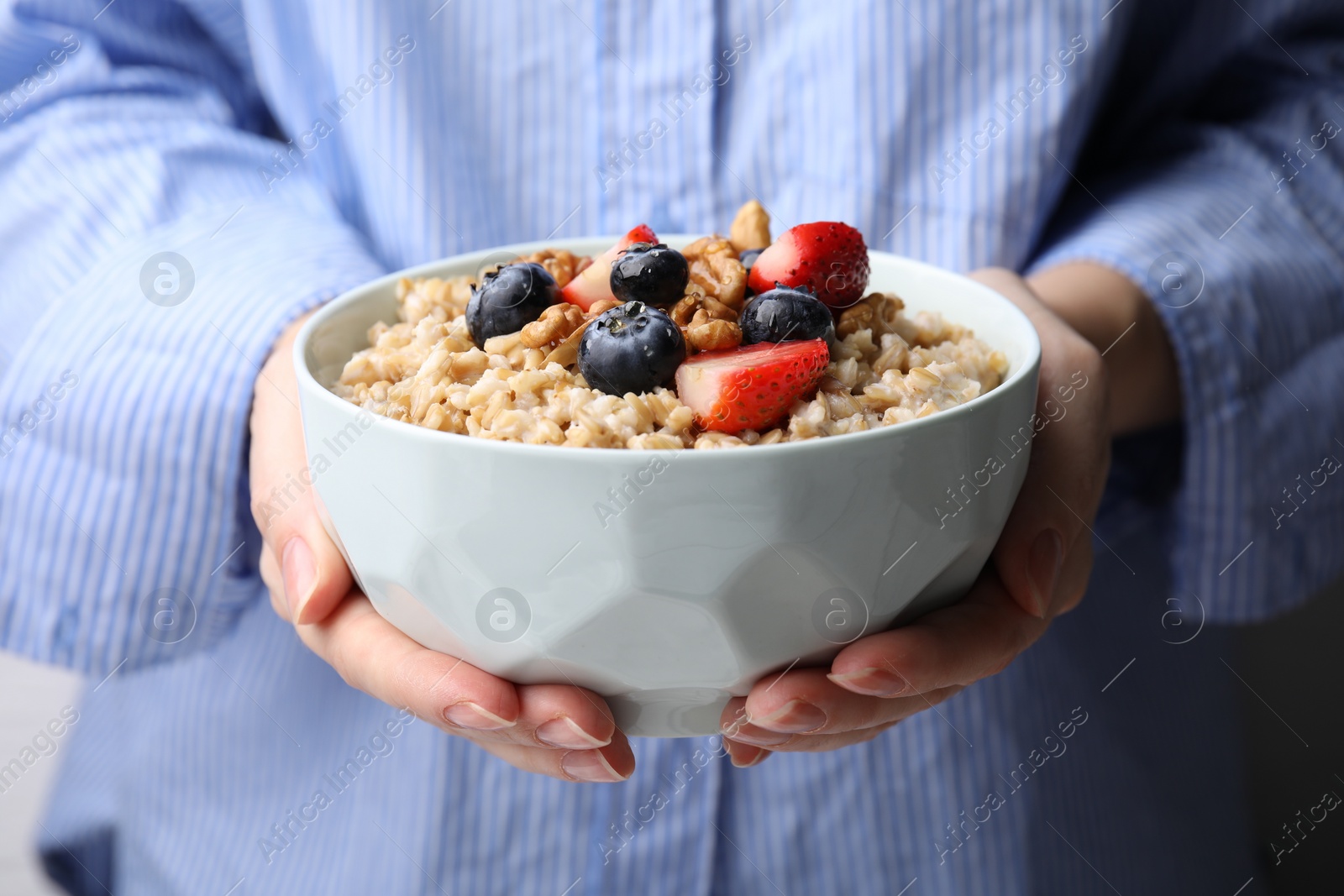 Photo of Woman holding bowl of tasty oatmeal with strawberries, blueberries and walnuts, closeup