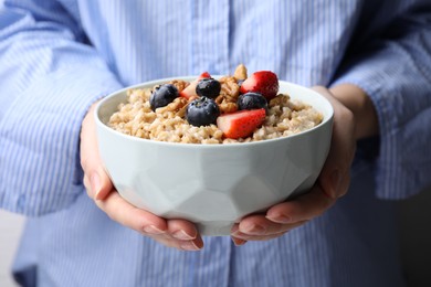 Photo of Woman holding bowl of tasty oatmeal with strawberries, blueberries and walnuts, closeup