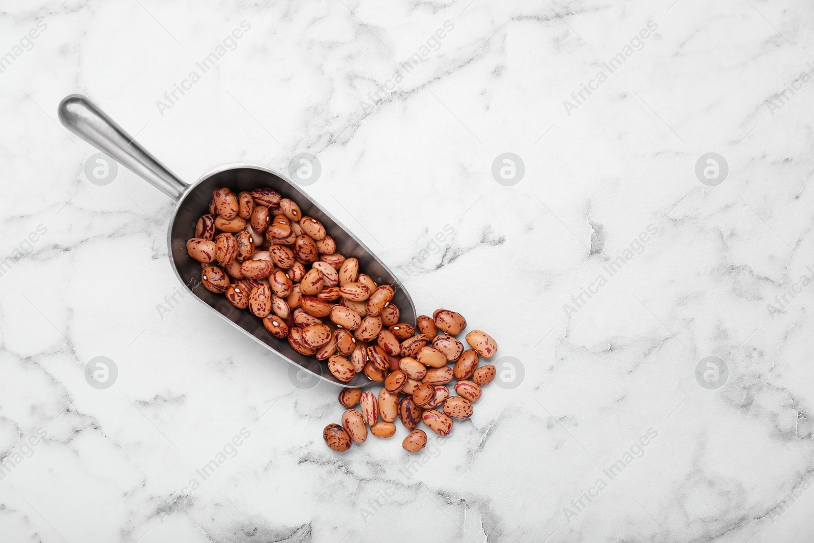 Photo of Metal scoop with dry kidney beans on white marble table, flat lay. Space for text