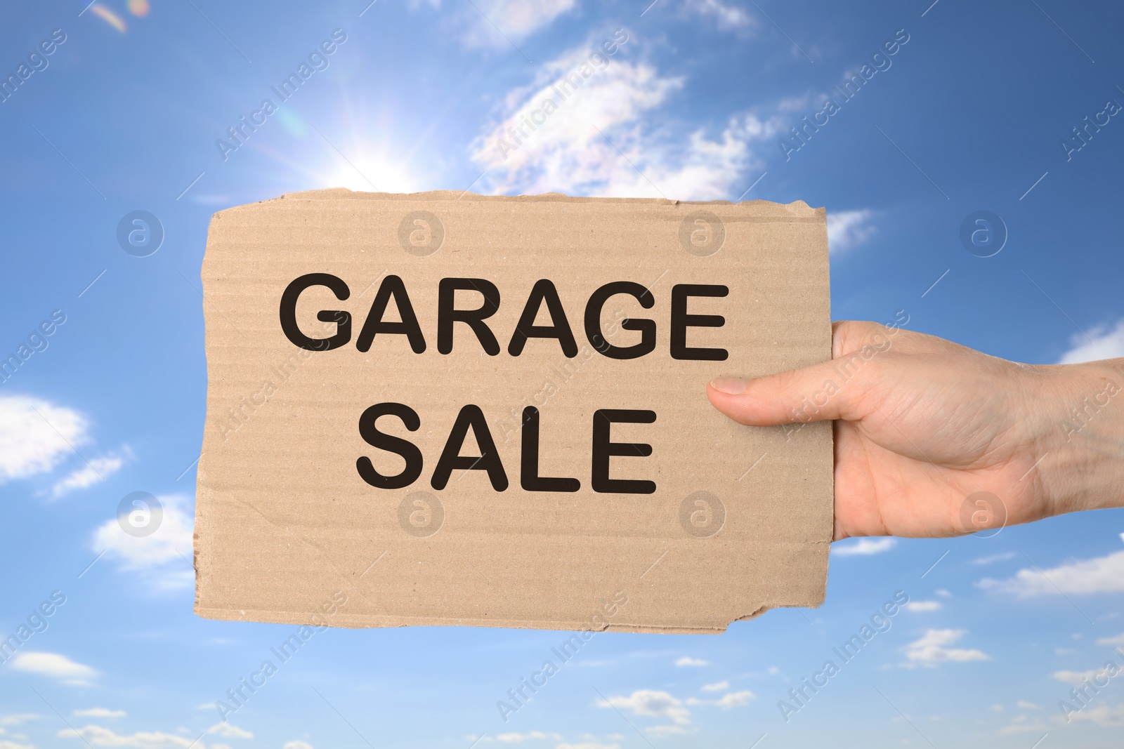 Image of Woman holding sign with text GARAGE SALE against blue sky