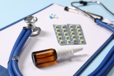 Photo of Stethoscope, pills, nasal spray and clipboard on light blue background, closeup. Medical tool