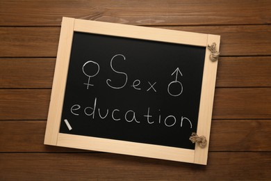 Image of Small black chalkboard with words Sex Education, female and male gender signs on wooden background, top view