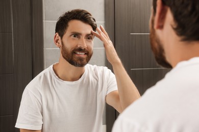 Photo of Handsome bearded man looking at mirror in bathroom