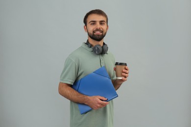 Student with headphones, folder and paper cup of coffee on grey background
