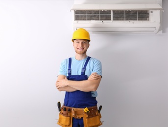 Professional technician near modern air conditioner indoors