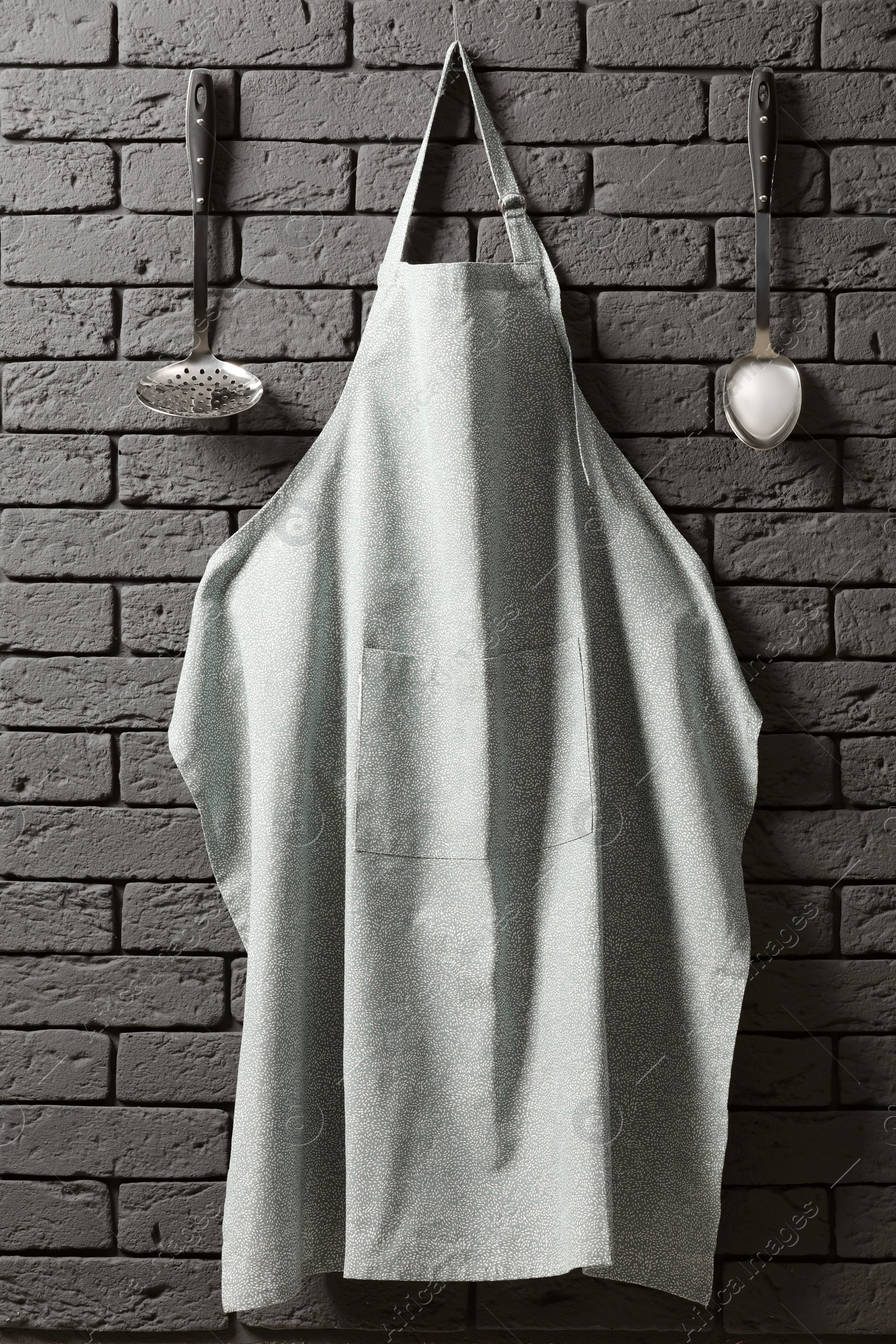 Photo of Clean apron with pattern and kitchen tools on grey brick wall