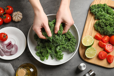 Photo of Woman cooking tasty kale salad on grey table, top view