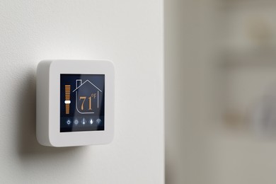 Image of Thermostat displaying temperature in Fahrenheit scale and different icons. Smart home device on white wall, space for text