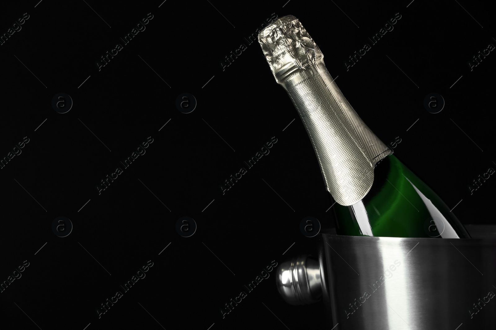 Photo of Bottle of champagne in bucket on black background. Space for text
