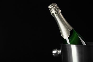 Bottle of champagne in bucket on black background. Space for text