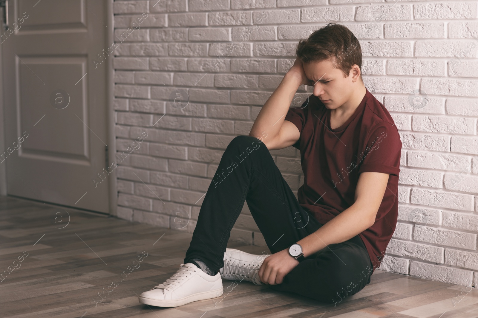 Photo of Upset teenage boy sitting alone on floor near wall