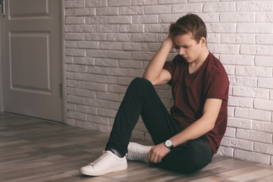 Upset teenage boy sitting alone on floor near wall