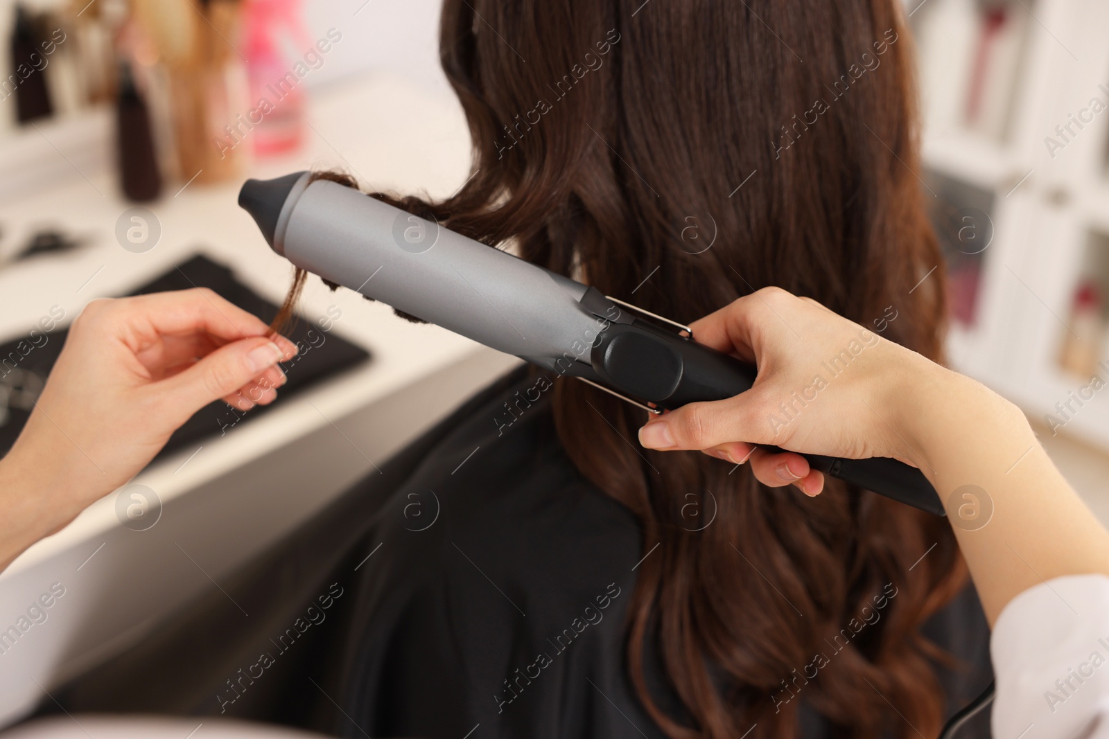 Photo of Hairdresser working with client using curling hair iron in salon, closeup