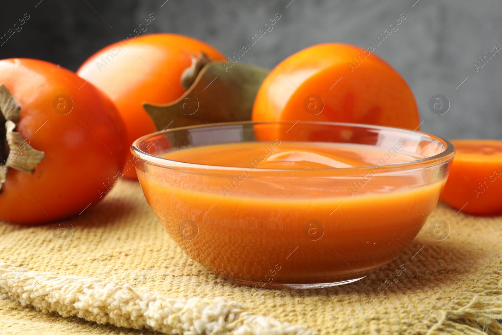 Photo of Delicious persimmon jam in glass bowl and fresh fruits on table, closeup