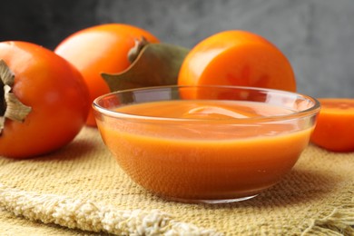 Delicious persimmon jam in glass bowl and fresh fruits on table, closeup