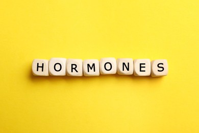 Photo of Word Hormones made of wooden cubes with letters on yellow background, flat lay