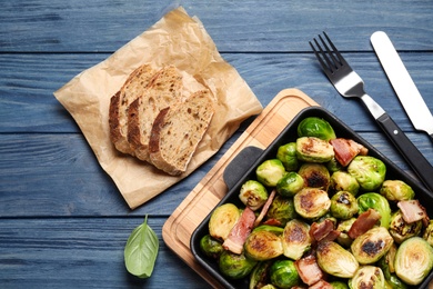 Photo of Delicious Brussels sprouts with bacon in baking pan on blue wooden table, flat lay