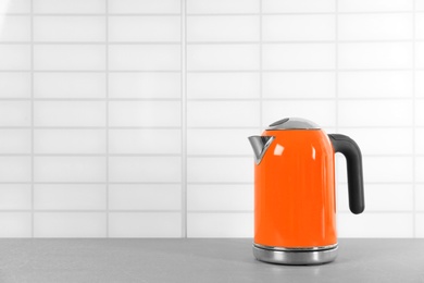 Photo of Stylish electric kettle on grey table against white wall, space for text. Tea preparation
