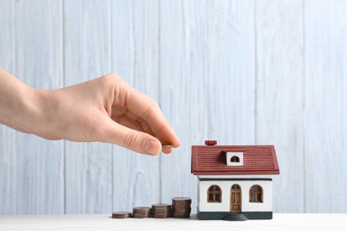 Woman putting coin near house model on table against wooden background. Space for text