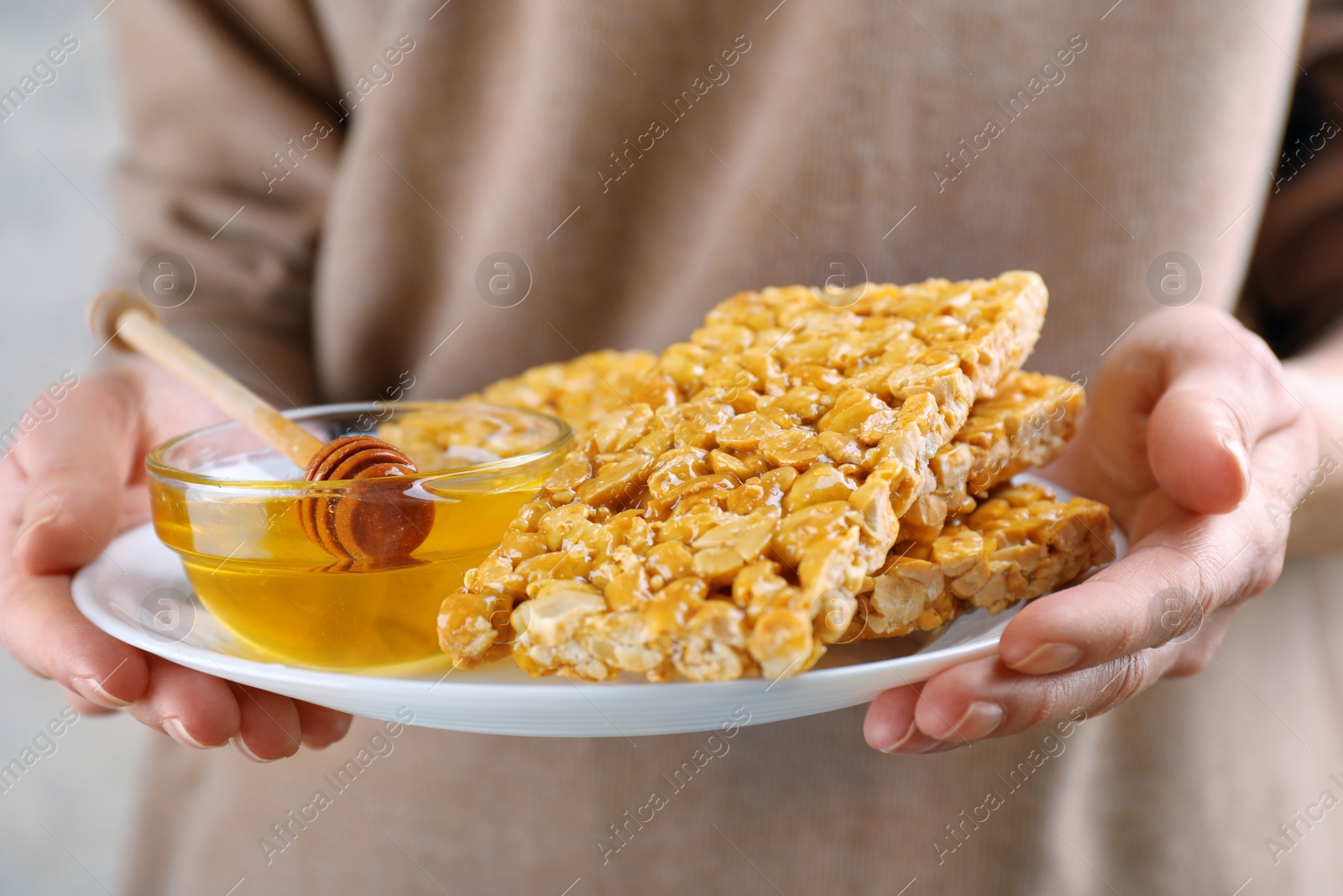 Photo of Woman holding bowl with delicious peanut kozinaki bars and honey, closeup