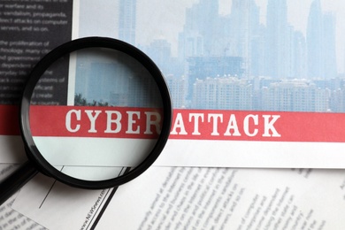 Newspaper with headline CYBER ATTACK and magnifying glass, top view