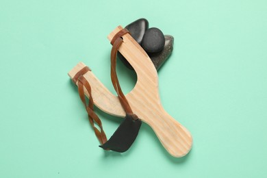 Wooden slingshot with stones on light green background, top view