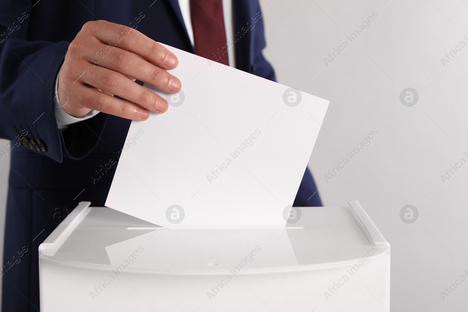 Photo of Man putting his vote into ballot box on light grey background, closeup