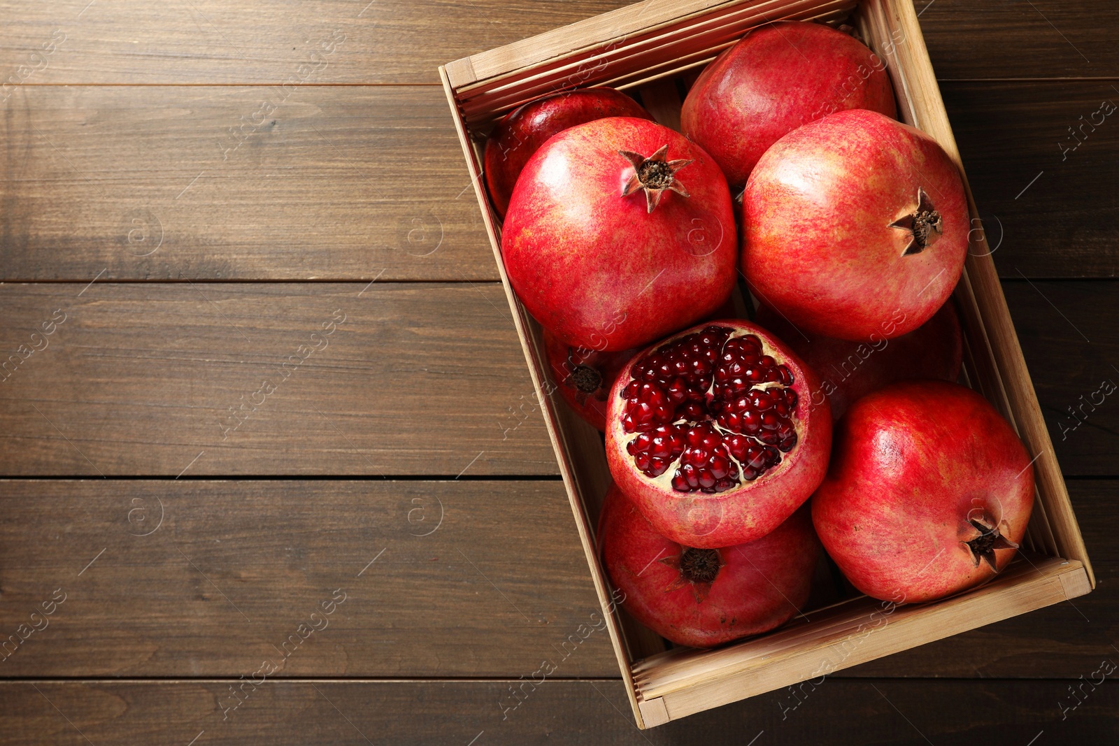 Photo of Ripe pomegranates in crate on wooden table, top view. Space for text