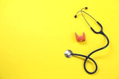 Photo of Endocrinology. Stethoscope and model of thyroid gland on yellow background, top view. Space for text