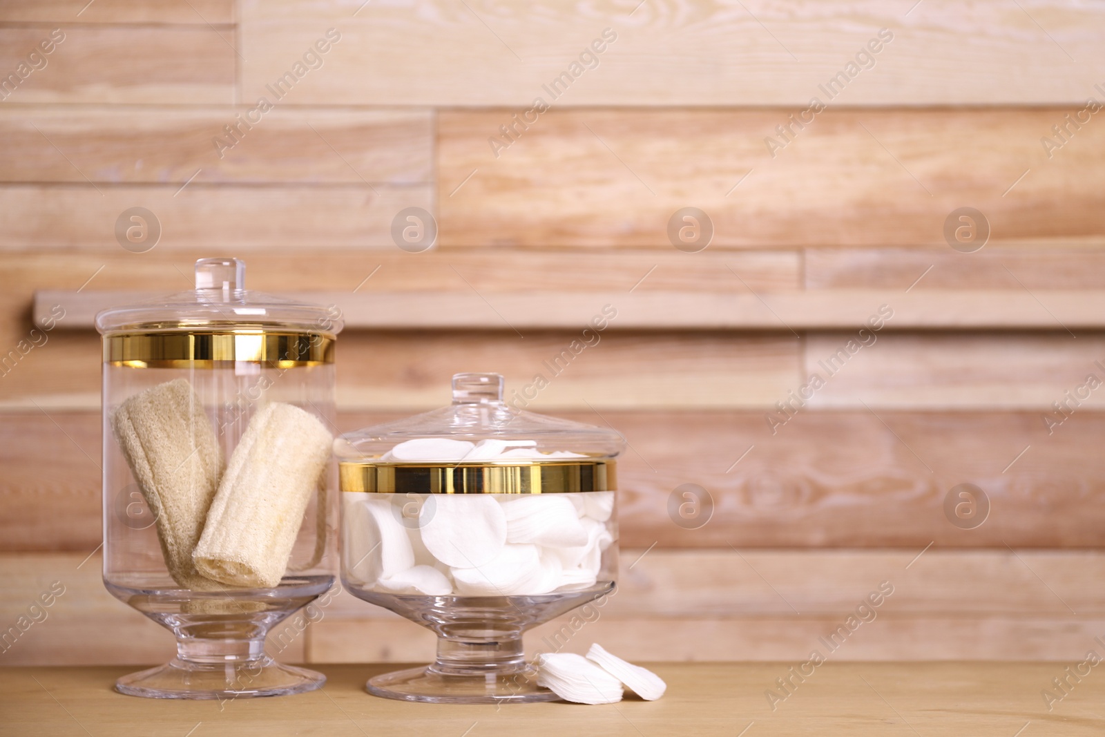 Photo of Composition of glass jar with cotton pads on table near wooden wall. Space for text