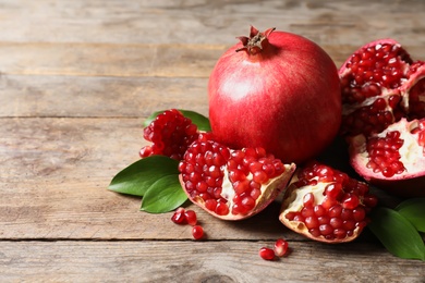 Ripe pomegranates and leaves on wooden background. Space for text