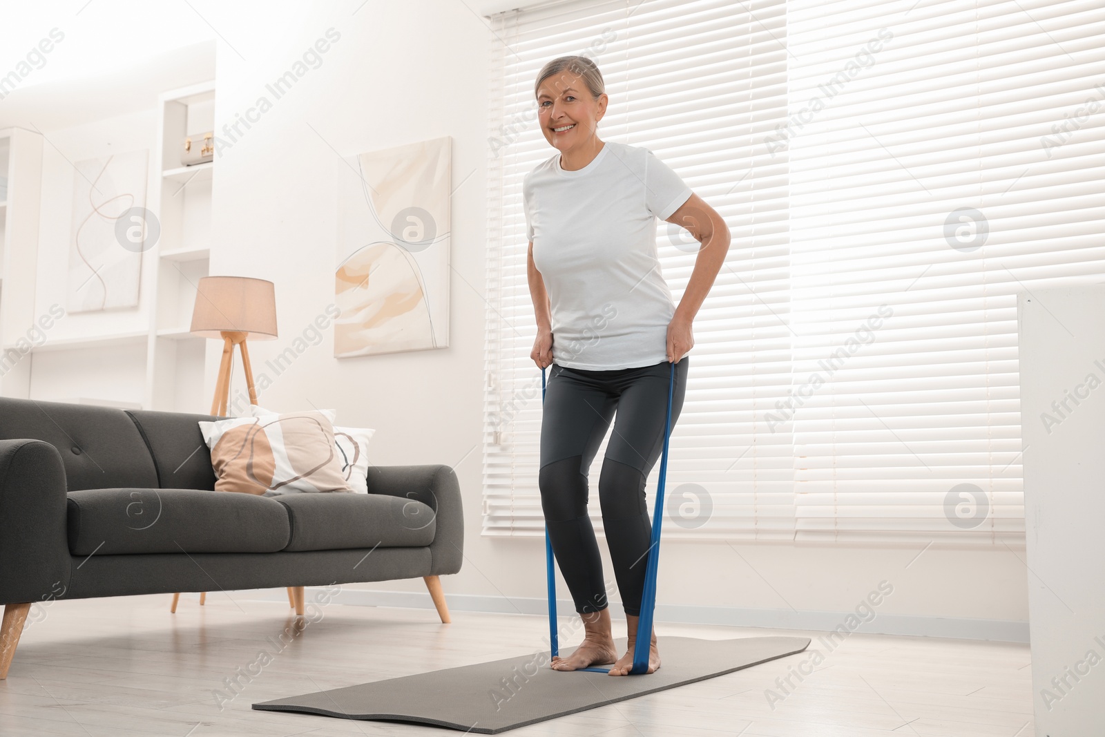 Photo of Senior woman doing exercise with fitness elastic band on mat at home