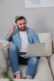 Photo of Man with laptop and headphones sitting on sofa at home