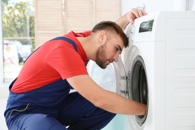 Young plumber examining washing machine in bathroom