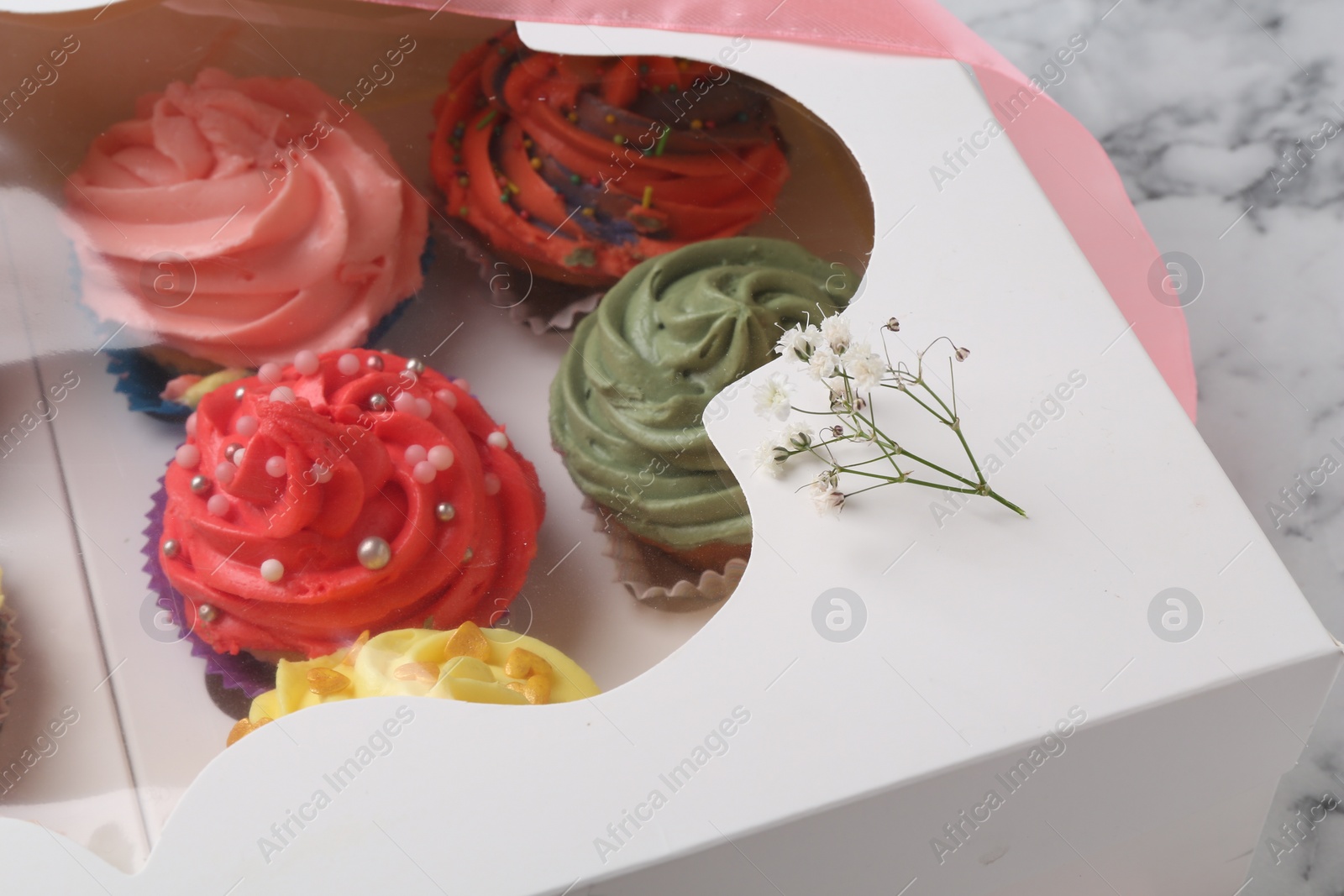 Photo of Different colorful cupcakes in box on table, closeup