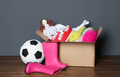 Donation box, shoes, toys and clothes on table near grey wall