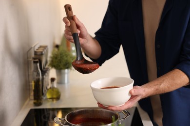 Man pouring delicious tomato soup into bowl in kitchen, closeup