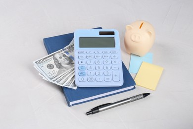 Photo of Calculator, dollar banknotes, piggy bank, notebook, sticky notes and pen on light gray table. Retirement concept