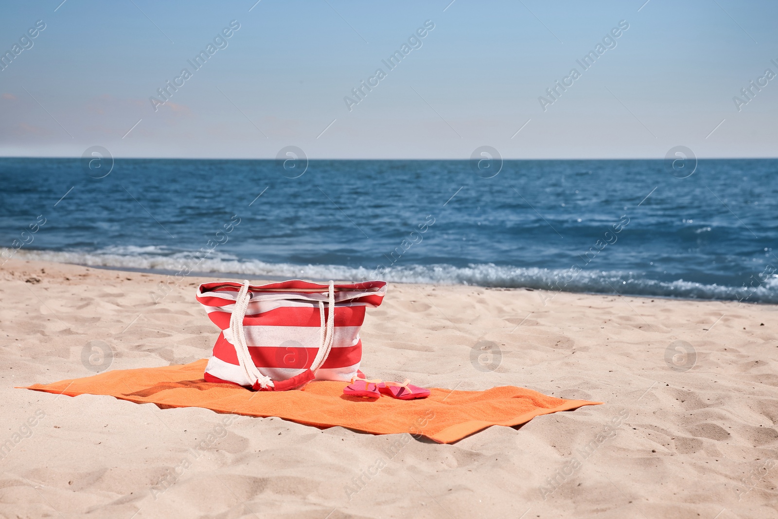 Photo of Soft orange beach towel, bag and flip flops on sandy seashore