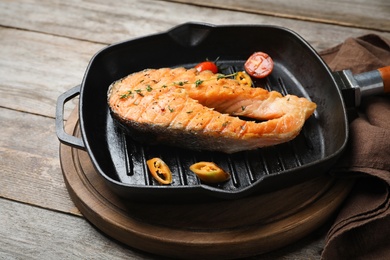 Photo of Frying pan with tasty salmon steak on wooden background