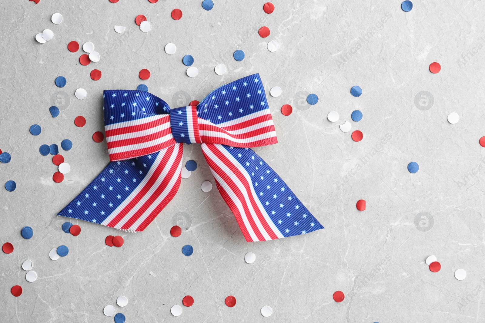 Photo of Ribbon bow with American flag pattern and confetti on light background, flat lay with space for text. USA Independence Day