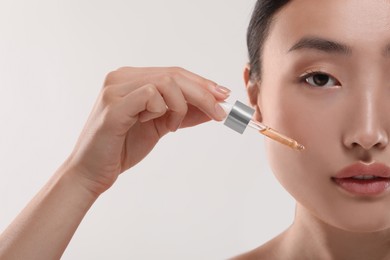 Photo of Beautiful young woman applying cosmetic serum onto her face on white background, closeup