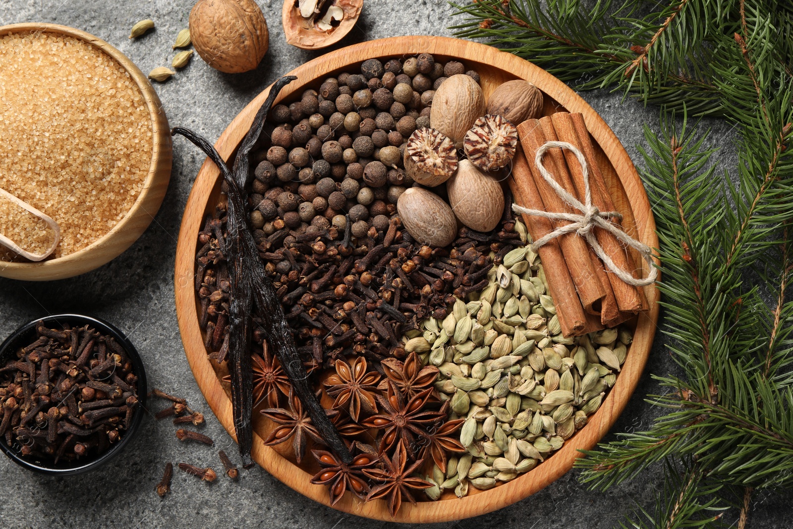 Photo of Different spices, nuts and fir branches on gray textured table, flat lay