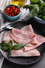 Photo of Tasty ham with basil, pickled peppers and carving fork on table